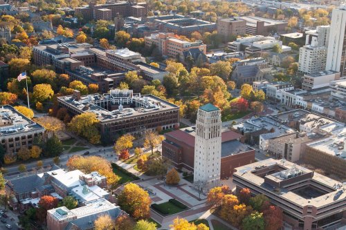 Aerial view of a university campus with colorful autumn trees and buildings, including a clock tower.