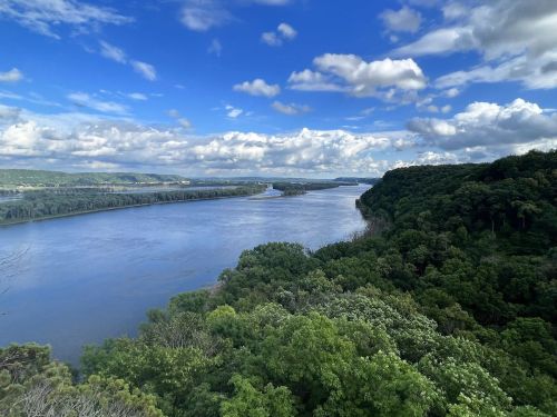 A scenic view of a river winding through lush green trees under a partly cloudy sky.