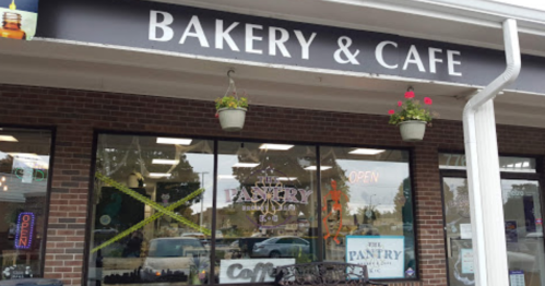 Exterior of a bakery and café with a sign reading "The Pantry," featuring hanging plants and an "Open" sign.