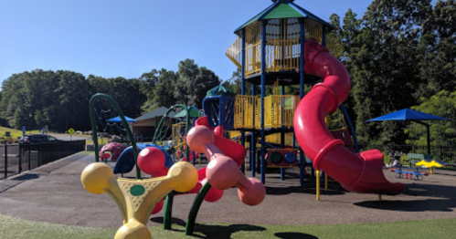 Colorful playground with slides and climbing structures, surrounded by green trees and sunny blue skies.