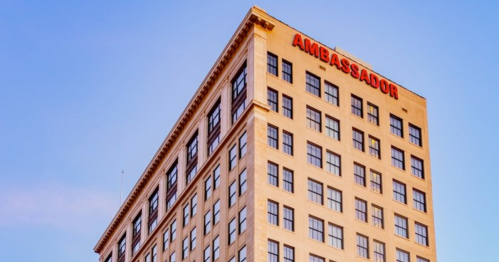 A tall building with the word "AMBASSADOR" prominently displayed on the top, against a clear blue sky.