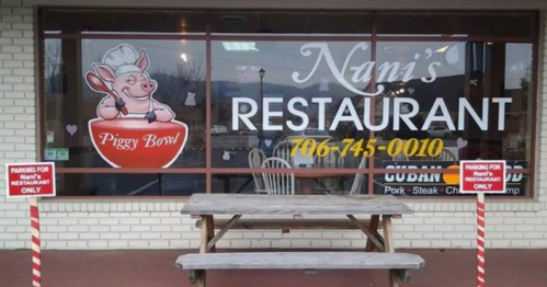 Sign for "Nana's Restaurant" featuring a pig mascot, with a picnic table outside and a phone number displayed.