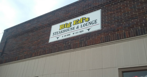 Sign for Big Ed's Steakhouse & Lounge on a brick building, featuring the restaurant's name and coordinates.