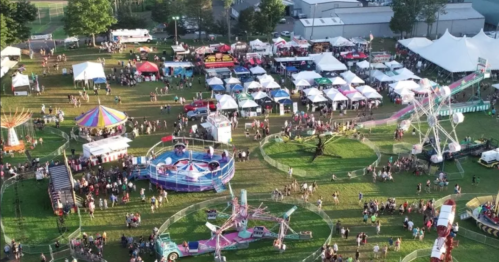 Aerial view of a lively fair with rides, food stalls, and crowds enjoying the festivities on a sunny day.