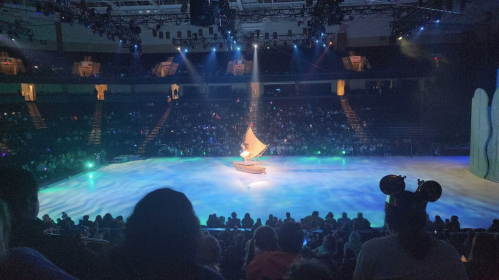 A stage with a boat and a colorful light display, surrounded by an audience in a large arena.