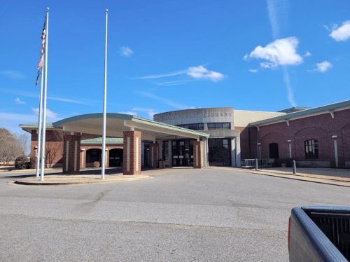 Exterior view of a public library building with flags, a covered entrance, and a clear blue sky.
