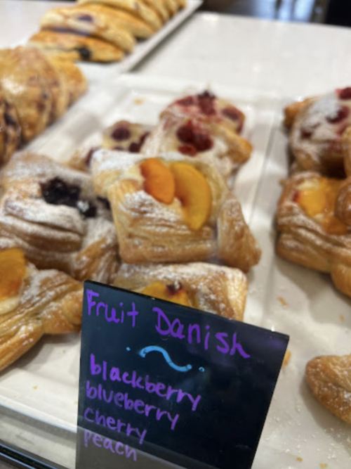 A display of fruit danishes with a sign listing flavors: blackberry, blueberry, cherry, and peach.