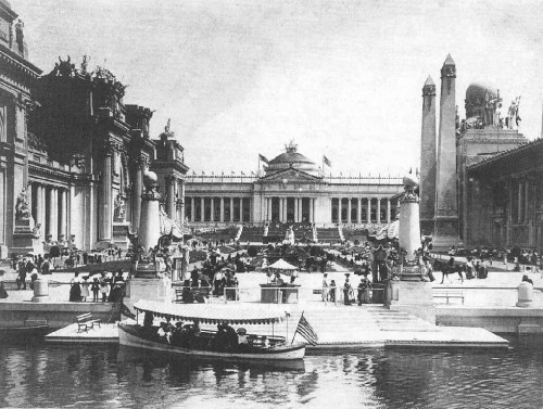 Historic black-and-white photo of a grand exhibition building with crowds and a boat in the foreground.