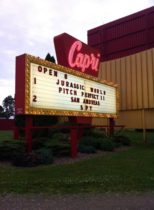 A vintage movie theater marquee displaying showtimes for "Jurassic World," "Pitch Perfect 2," "San Andreas," and "Spy."