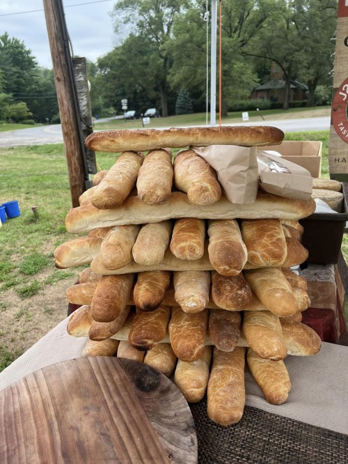 A tall stack of freshly baked baguettes displayed outdoors on a table.