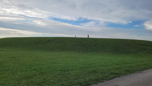 A grassy hill under a cloudy sky, with two small figures standing at the top.