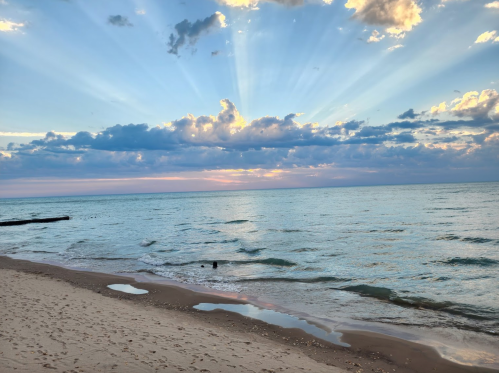 A serene beach scene at sunset, with rays of sunlight breaking through clouds over calm waters.