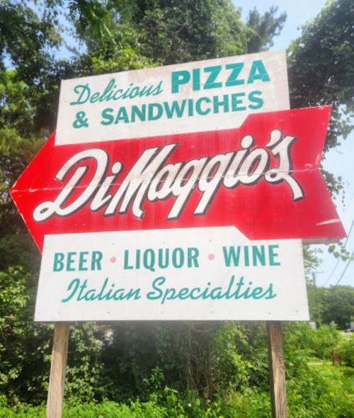 Sign for DiMaggio's featuring pizza, sandwiches, beer, liquor, wine, and Italian specialties, with a red arrow.