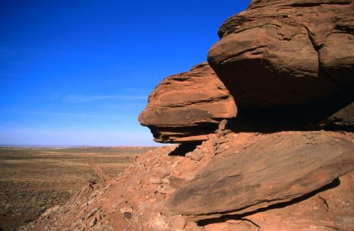 A rocky landscape with a large sandstone formation under a clear blue sky, stretching into the distance.