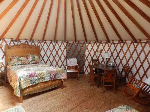 Cozy interior of a yurt featuring a bed, dining table, and wooden chairs with a rustic wooden floor.