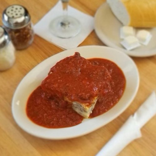 A plate of meatloaf topped with marinara sauce, served with a side of bread and condiments on a wooden table.