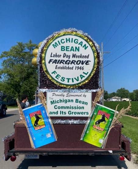 A float for the Michigan Bean Festival, featuring a large sign and colorful banners, celebrating the event's history.