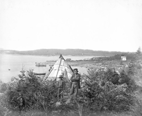 Two individuals stand near a teepee by a body of water, with trees and a distant settlement visible in the background.