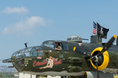 A vintage bomber aircraft with "Executive Sweet" painted on the side, featuring a pin-up girl design and flags on top.
