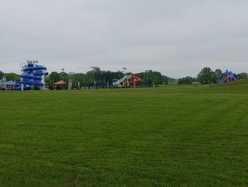 A grassy field with water slides in the background under a cloudy sky.