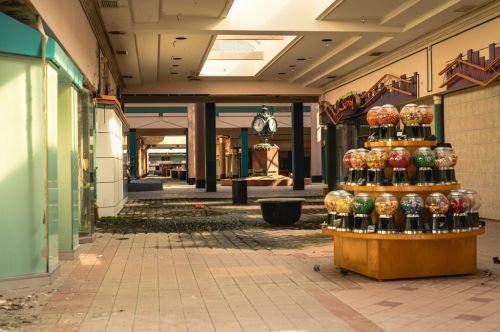 Abandoned mall interior with a colorful gumball machine in the foreground and empty storefronts in the background.