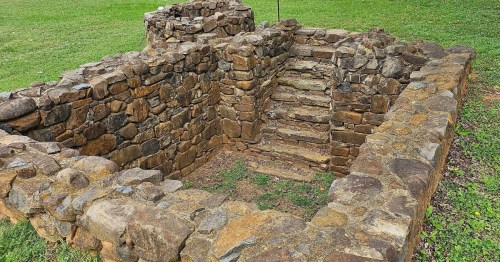 Stone ruins with stairs, surrounded by grass, showcasing an ancient structure in a natural setting.