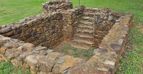 Stone ruins with stairs, surrounded by grass, showcasing an ancient structure in a natural setting.