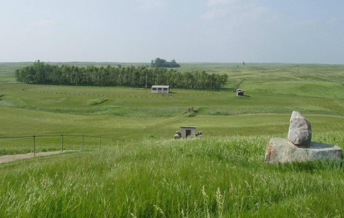 A serene landscape featuring rolling green hills, a small building, and a large rock in the foreground.