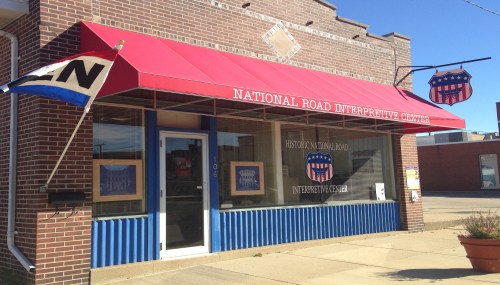 Exterior of the National Road Interpretive Center, featuring a red awning and blue accents on a brick building.