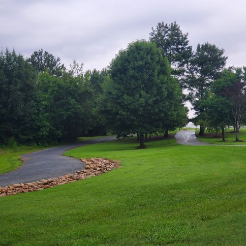 A winding gravel path through a lush green park with trees and grass on either side.