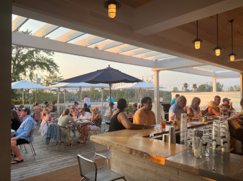 A lively outdoor bar and dining area with patrons enjoying drinks and meals under umbrellas during sunset.