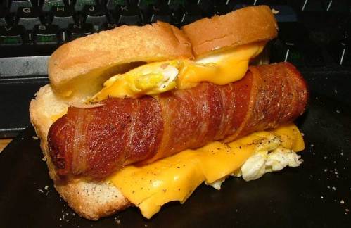 A sandwich with layers of bacon, cheese, and an egg, served on toasted bread, with a keyboard in the background.