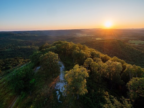 A scenic view of rolling hills and trees at sunset, with warm colors illuminating the landscape.