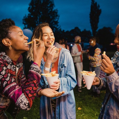 A group of friends enjoying food outdoors during twilight, smiling and chatting in a lively atmosphere.