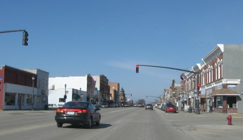 A view of a small town street with a red traffic light and historic buildings lining the road under a clear blue sky.