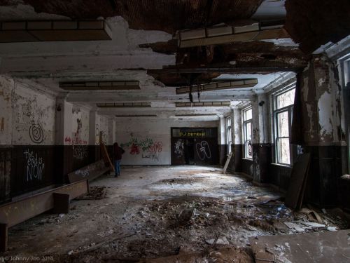 Abandoned room with graffiti, broken windows, and debris on the floor, creating a desolate atmosphere.