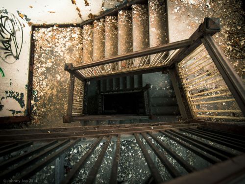 Aerial view of a worn staircase in an abandoned building, with debris scattered on the steps and walls.