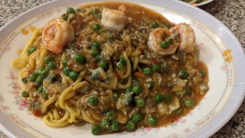 A plate of pasta topped with shrimp, green peas, and a savory sauce, served on a floral-patterned dish.