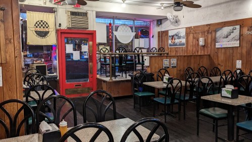 A cozy restaurant interior with empty tables and chairs, wooden walls, and a red door, creating a welcoming atmosphere.