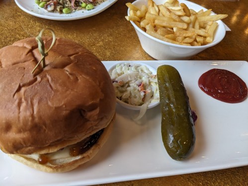 A plate featuring a burger with a pickle, coleslaw, fries, and ketchup on a golden table.