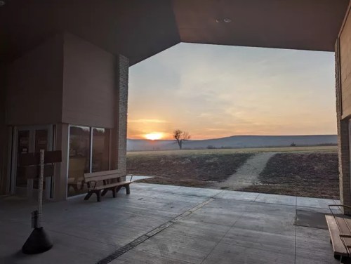 A sunset view from a building entrance, with a tree and open field in the background.