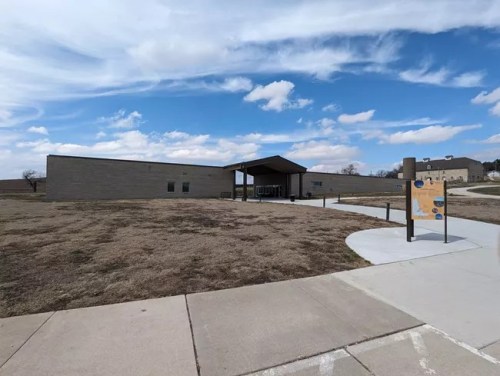 A modern building with a sloped roof, surrounded by grass and a pathway, under a partly cloudy sky.