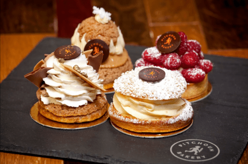 A selection of elegant pastries on a slate platter, featuring cream, chocolate, and raspberry toppings.