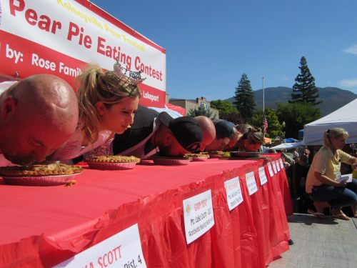 Participants compete in a pie-eating contest at the Kelseyville Pear Festival, with pies on a table and spectators watching.