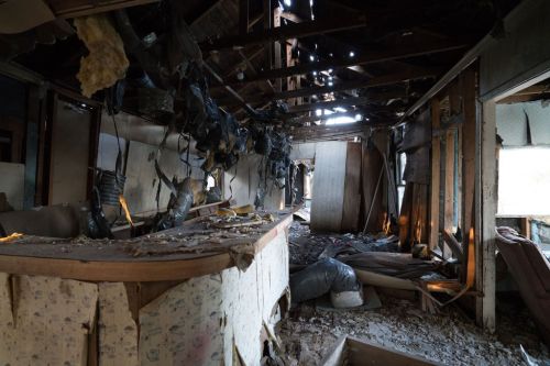 Interior of a dilapidated room with exposed beams, debris, and damaged walls, creating a scene of neglect and decay.