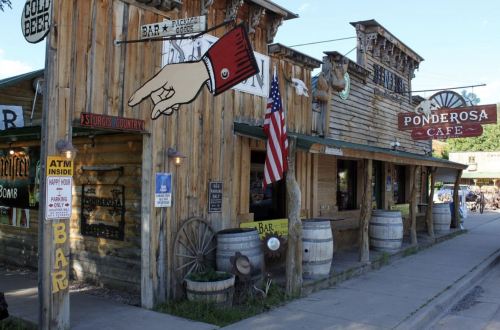 A rustic wooden building with a sign pointing to "Ponderosa Café," featuring barrels and an American flag outside.