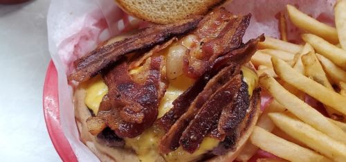 A close-up of a cheeseburger topped with crispy bacon, served with a side of golden French fries.
