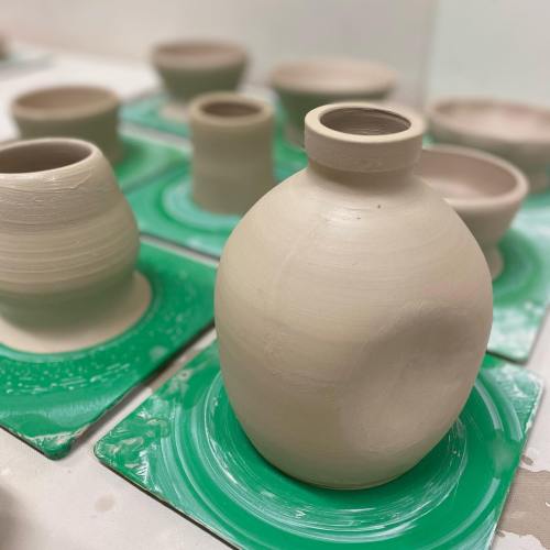 A collection of unglazed pottery pieces on green pottery wheels, showcasing various shapes and sizes.
