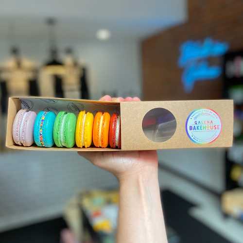 A hand holds a box of colorful macarons from Galena Bakehouse, showcasing a variety of vibrant flavors.