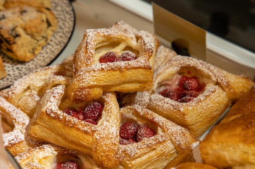 A close-up of flaky pastries filled with raspberries and dusted with powdered sugar, displayed in a bakery.